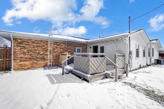 snow covered rear of property with cooling unit, brick siding, fence, and a wooden deck