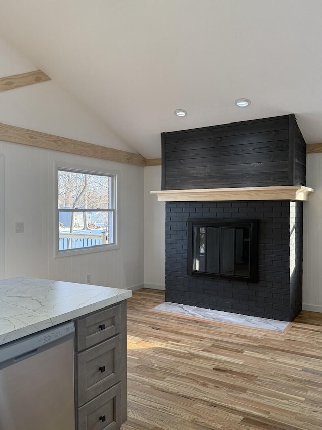 kitchen with lofted ceiling, a brick fireplace, light wood-type flooring, stainless steel dishwasher, and light stone countertops