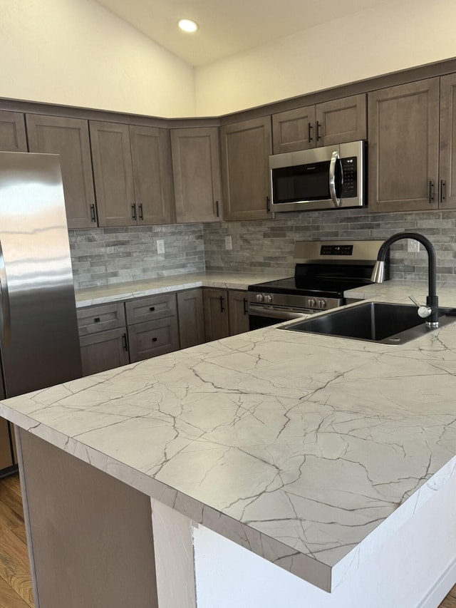 kitchen featuring sink, backsplash, stainless steel appliances, wood-type flooring, and vaulted ceiling