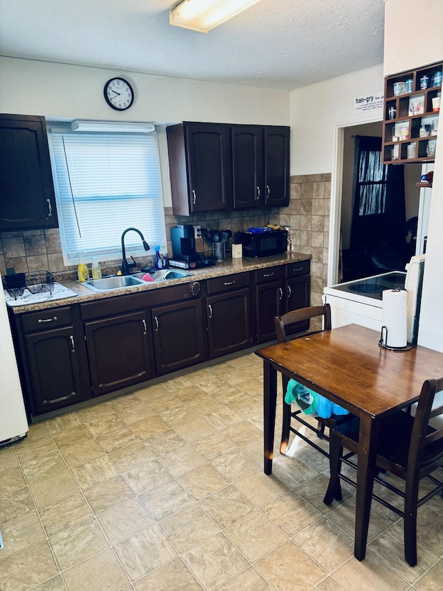 kitchen with tasteful backsplash, a sink, a textured ceiling, light stone countertops, and black microwave