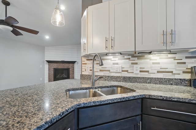 kitchen with tasteful backsplash, a brick fireplace, white cabinets, a sink, and dark stone countertops