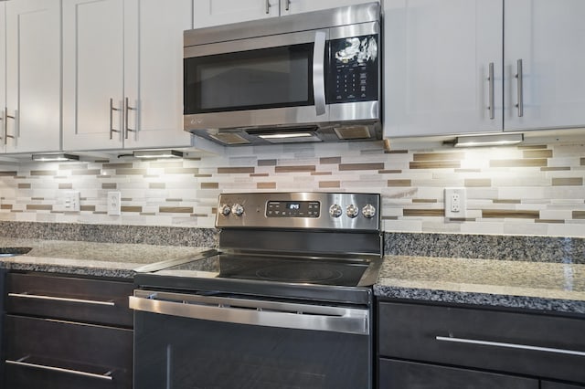 kitchen featuring stainless steel appliances, white cabinetry, backsplash, and light stone counters