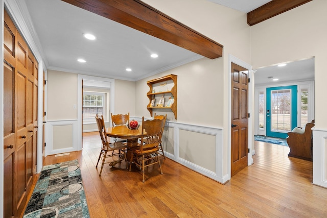 dining space featuring beam ceiling, a decorative wall, light wood-style floors, and ornamental molding