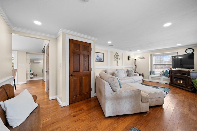 living room featuring recessed lighting, a lit fireplace, light wood-style flooring, and crown molding