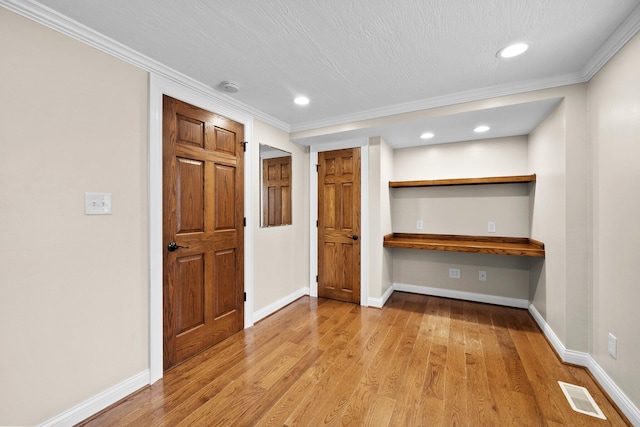 spare room with built in desk, baseboards, visible vents, and wood finished floors