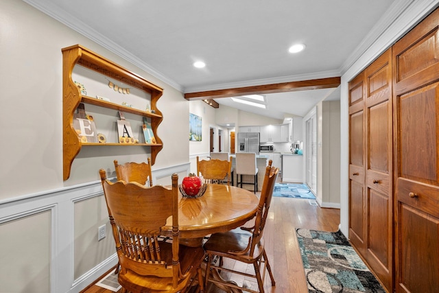 dining area featuring lofted ceiling, ornamental molding, light wood-style floors, wainscoting, and a decorative wall