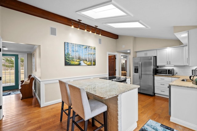 kitchen with light wood finished floors, a kitchen island, light stone countertops, lofted ceiling, and appliances with stainless steel finishes