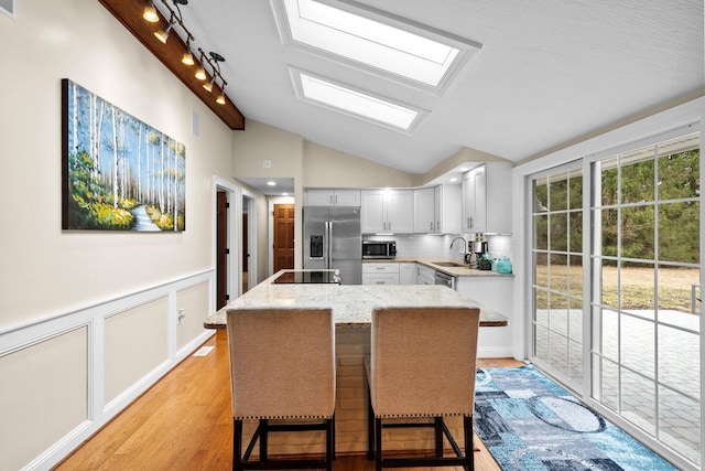 kitchen with a center island, light stone countertops, lofted ceiling with skylight, appliances with stainless steel finishes, and a sink