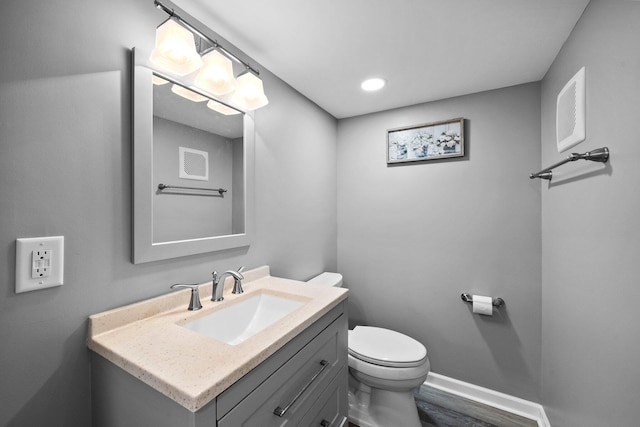 bathroom featuring visible vents, baseboards, toilet, wood finished floors, and vanity