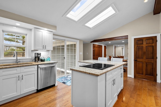 kitchen featuring light wood-type flooring, a sink, stainless steel dishwasher, vaulted ceiling with skylight, and black electric stovetop