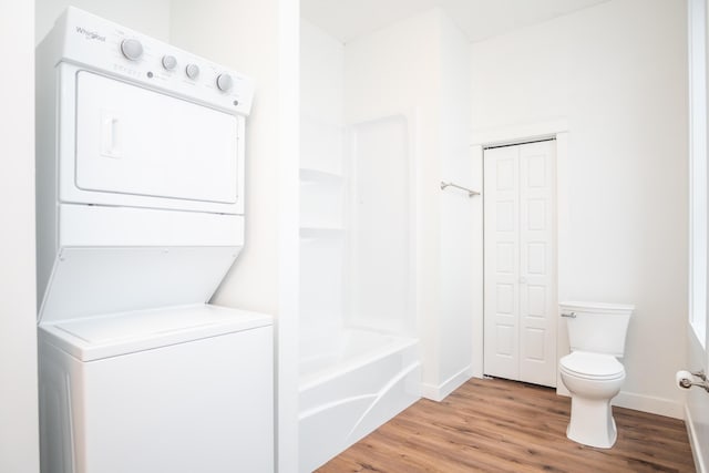 bathroom with hardwood / wood-style flooring, stacked washer and dryer, toilet, and a washtub