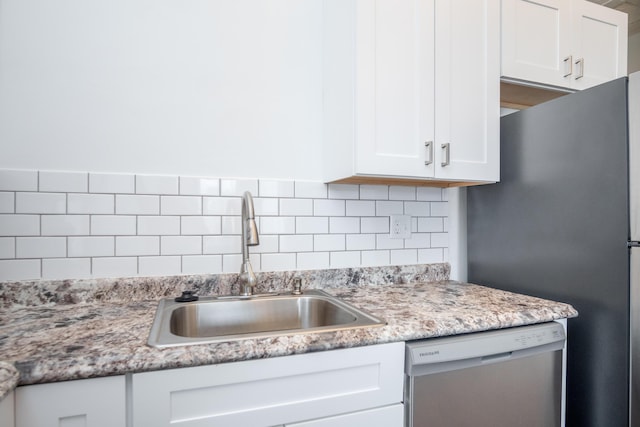 kitchen with sink, tasteful backsplash, stainless steel refrigerator, dishwashing machine, and white cabinets