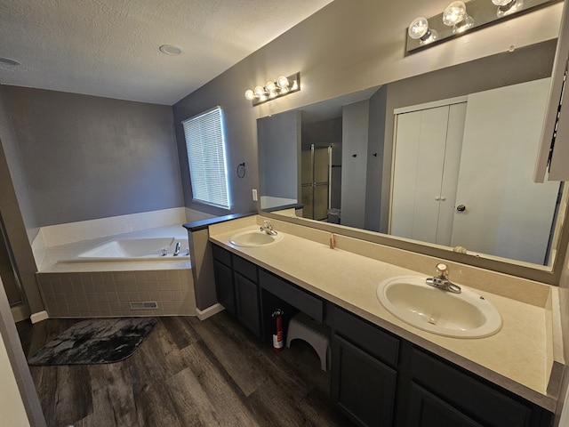 2973 Kicking Bird Trce, Dublin, OH 43017 - bathroom featuring wood finished floors, a textured ceiling, a bath, double vanity, and an enclosed shower
