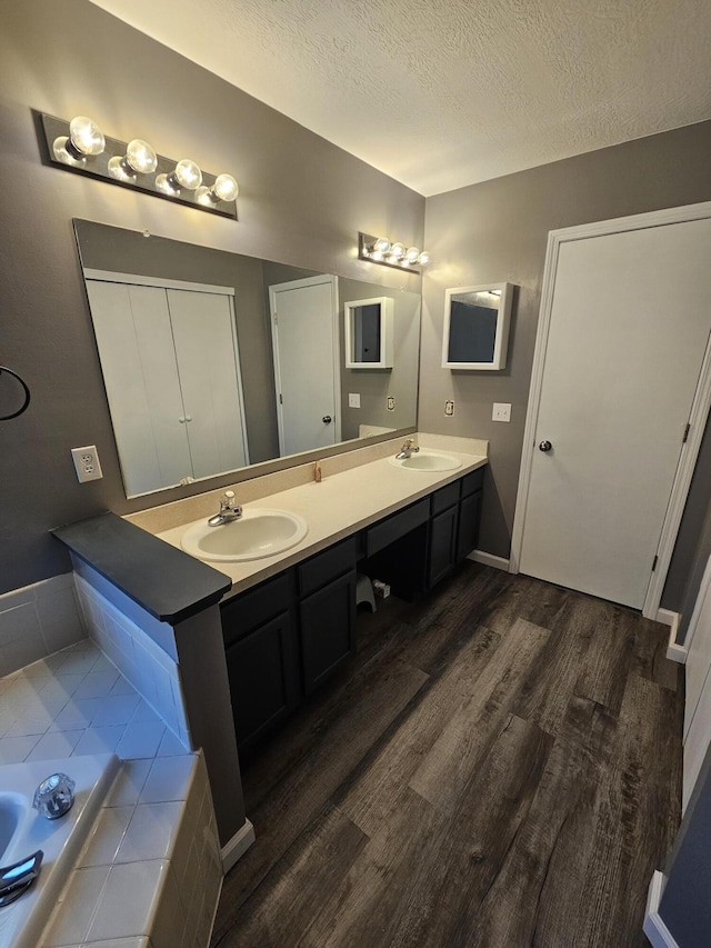 2973 Kicking Bird Trce, Dublin, OH 43017 - bathroom with wood finished floors, double vanity, a textured ceiling, and tiled tub