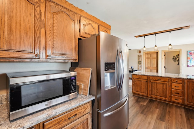 kitchen with stainless steel appliances, dark wood-style flooring, brown cabinets, light stone countertops, and decorative light fixtures