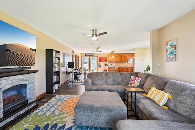 living room with baseboards, a stone fireplace, dark wood-style floors, and a ceiling fan