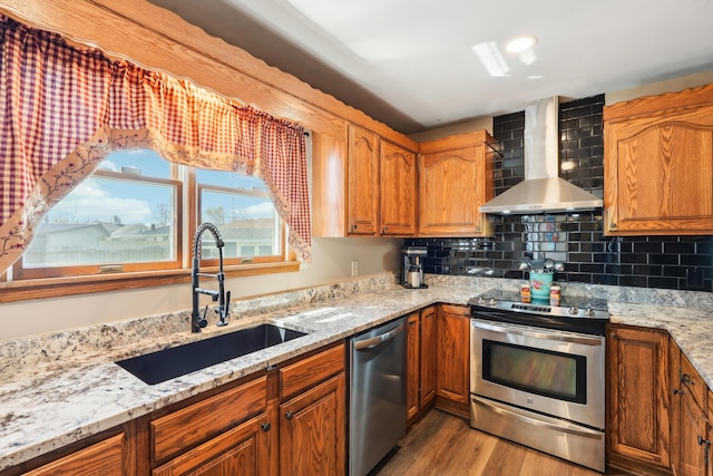 kitchen with stainless steel appliances, wood finished floors, wall chimney range hood, a sink, and brown cabinetry