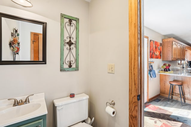 half bath with wood finished floors, toilet, and vanity