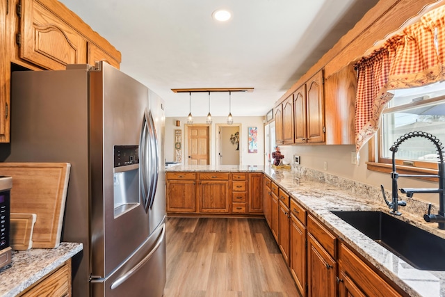 kitchen with stainless steel fridge with ice dispenser, wood finished floors, a sink, decorative light fixtures, and brown cabinetry