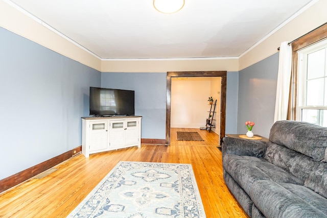 living area featuring baseboards, light wood-type flooring, and crown molding