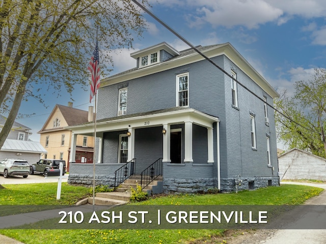 american foursquare style home featuring covered porch, a front yard, and brick siding