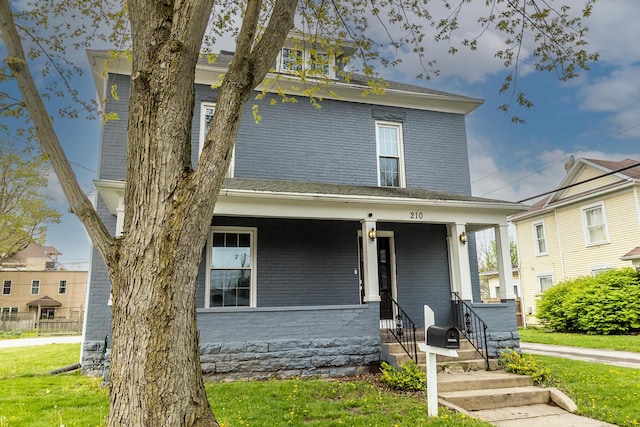 traditional style home featuring a front lawn, covered porch, and brick siding