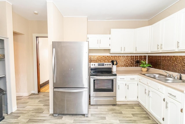kitchen with light wood-style floors, appliances with stainless steel finishes, white cabinets, backsplash, and a sink