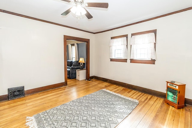 spare room with crown molding, visible vents, hardwood / wood-style floors, baseboards, and a ceiling fan