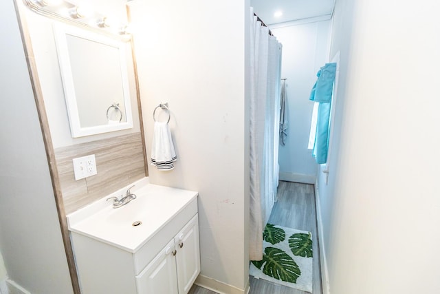 bathroom with wood finished floors, backsplash, vanity, and baseboards