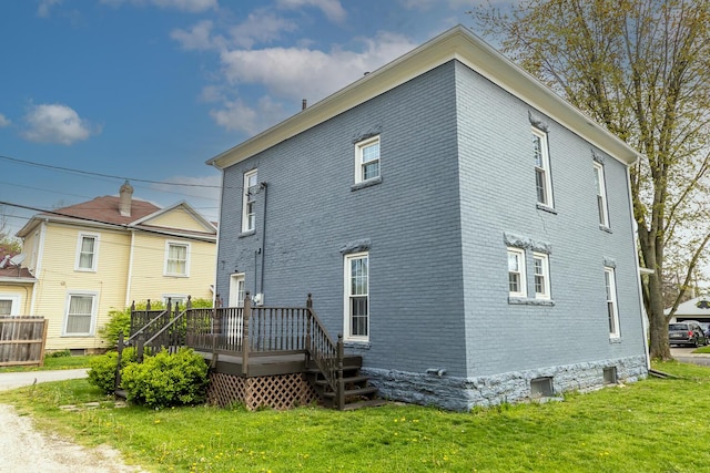 rear view of property featuring a lawn, a wooden deck, and brick siding