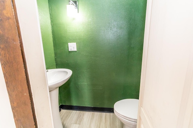 bathroom with baseboards, wood finished floors, and toilet