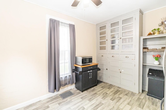 home office featuring light wood finished floors, a ceiling fan, visible vents, and baseboards