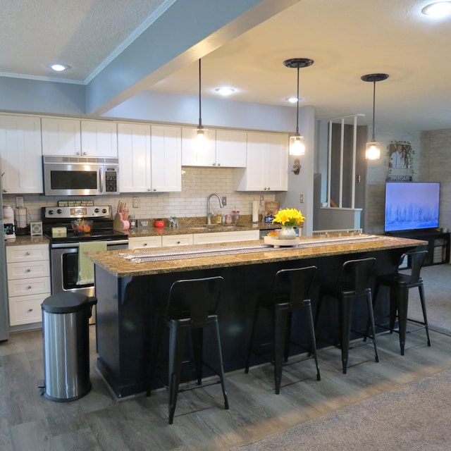 1084 Colonial Dr, Sidney, OH 45365 - kitchen featuring appliances with stainless steel finishes, crown molding, dark wood finished floors, a kitchen breakfast bar, and light stone counters