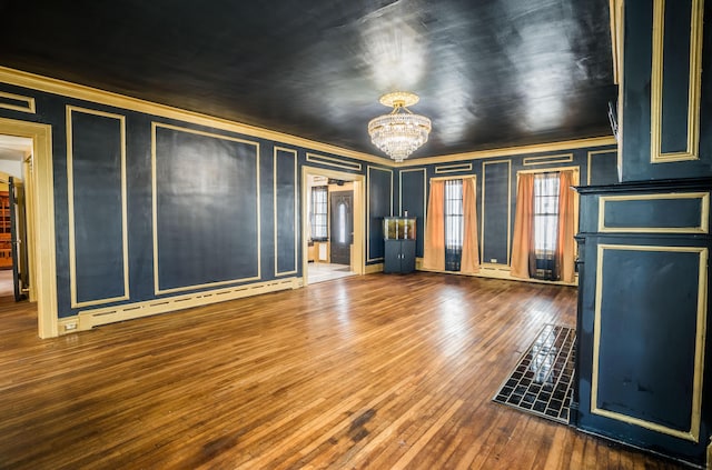unfurnished living room featuring a baseboard radiator, a decorative wall, crown molding, wood-type flooring, and a notable chandelier