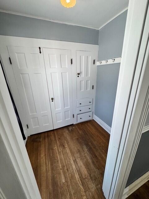 unfurnished bedroom featuring baseboards, a closet, dark wood-type flooring, and ornamental molding