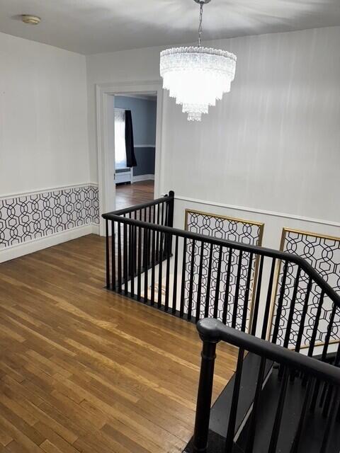 staircase featuring wood finished floors, baseboards, a notable chandelier, and wainscoting