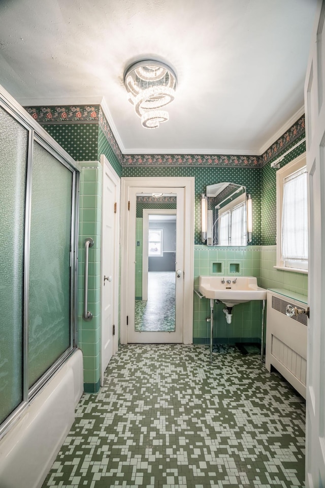 full bath featuring radiator heating unit, tile patterned floors, tile walls, and bath / shower combo with glass door