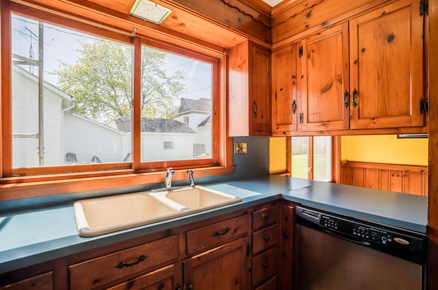kitchen featuring brown cabinets, stainless steel dishwasher, dark countertops, and a sink