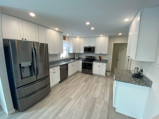 kitchen featuring a sink, light wood-style floors, white cabinets, appliances with stainless steel finishes, and dark stone counters