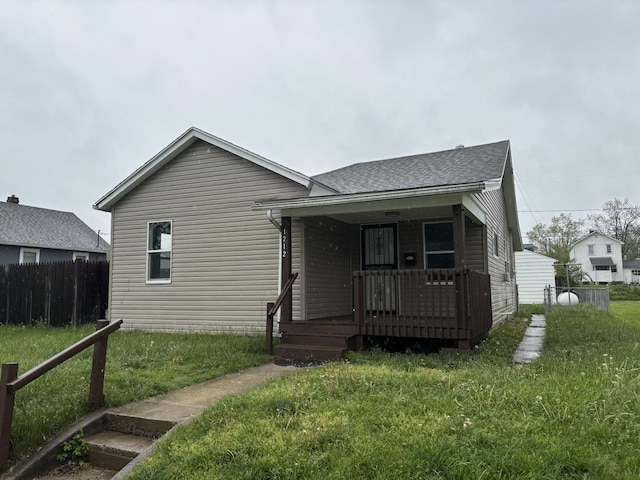 view of front of property featuring roof with shingles, fence, covered porch, and a front yard