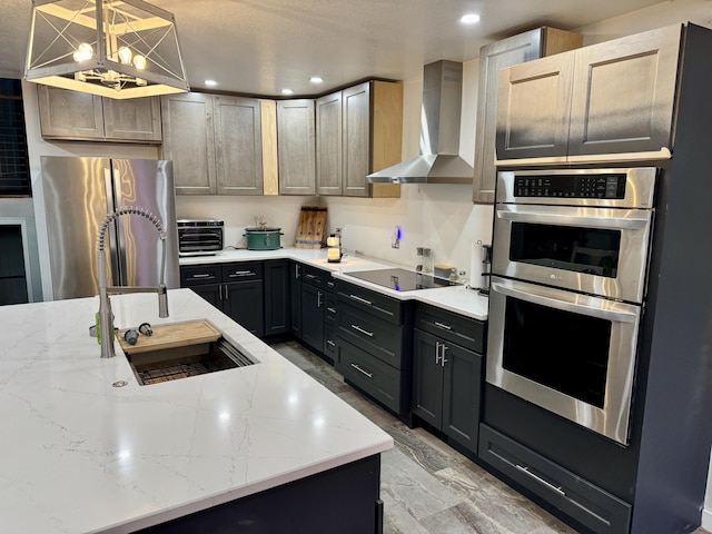 kitchen featuring appliances with stainless steel finishes, a sink, wall chimney range hood, and light stone countertops