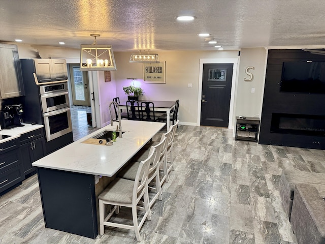 kitchen with a textured ceiling, stainless steel double oven, a sink, a kitchen bar, and pendant lighting