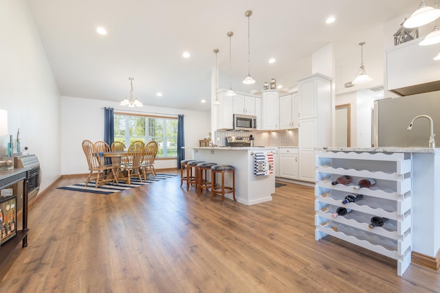 9342 State Route 368, Huntsville, OH 43324 - kitchen with stainless steel appliances, white cabinets, a kitchen bar, a chandelier, and backsplash