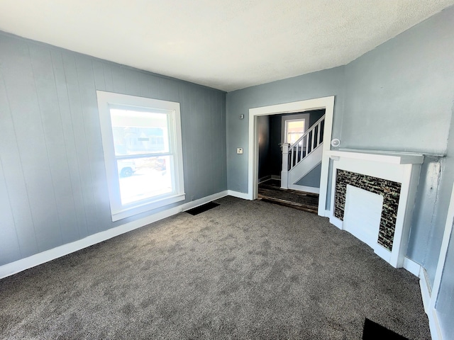 unfurnished living room featuring a wealth of natural light, a textured ceiling, and dark colored carpet