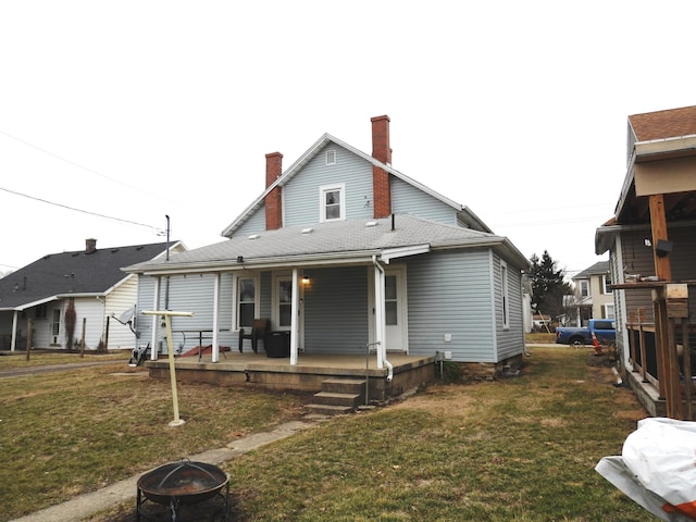 back of property with an outdoor fire pit, a yard, and covered porch