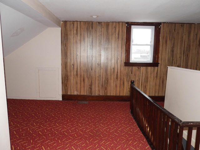 bonus room with lofted ceiling, wooden walls, and dark colored carpet