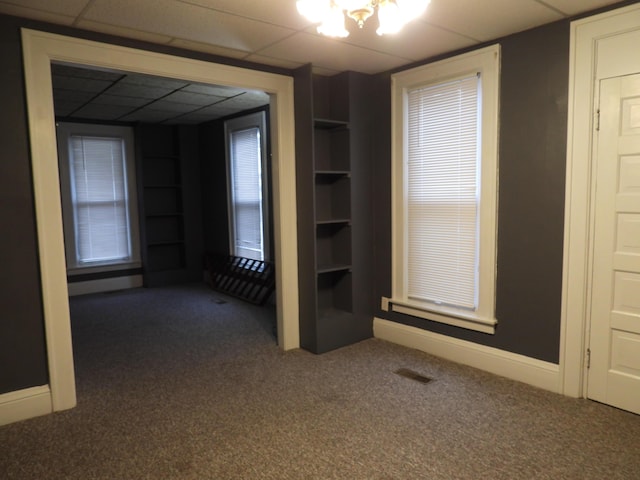 carpeted empty room with a paneled ceiling, a notable chandelier, and built in shelves