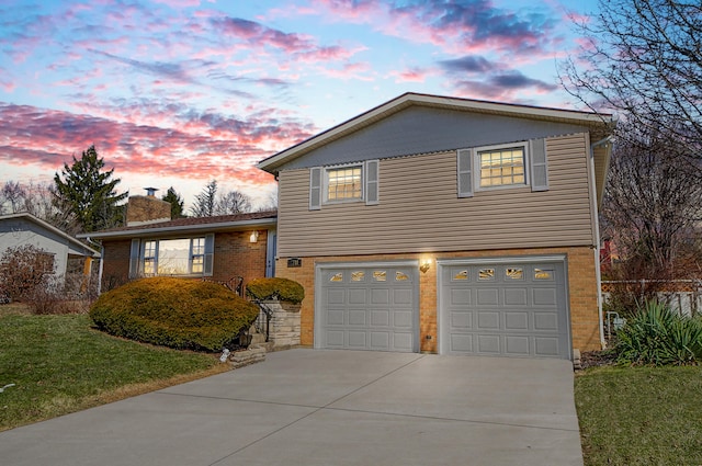 split level home featuring concrete driveway, a chimney, an attached garage, a front lawn, and brick siding