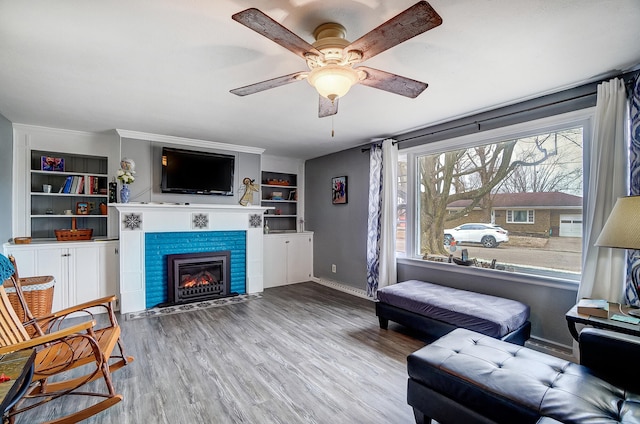 living area with ceiling fan, a tile fireplace, wood finished floors, baseboards, and built in features