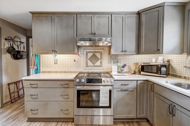 kitchen featuring light wood-style floors, stainless steel appliances, light countertops, under cabinet range hood, and a sink